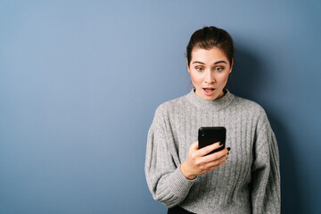 Young woman staring aghast at her mobile phone over blue