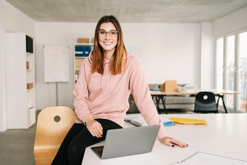 Friendly relaxed young businesswoman perched on desk
