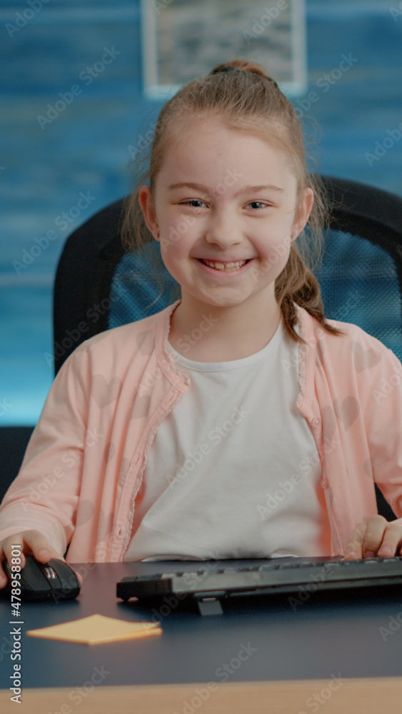 Poster portrait of schoolgirl at desk using computer and keyboard for online school courses and homework. l