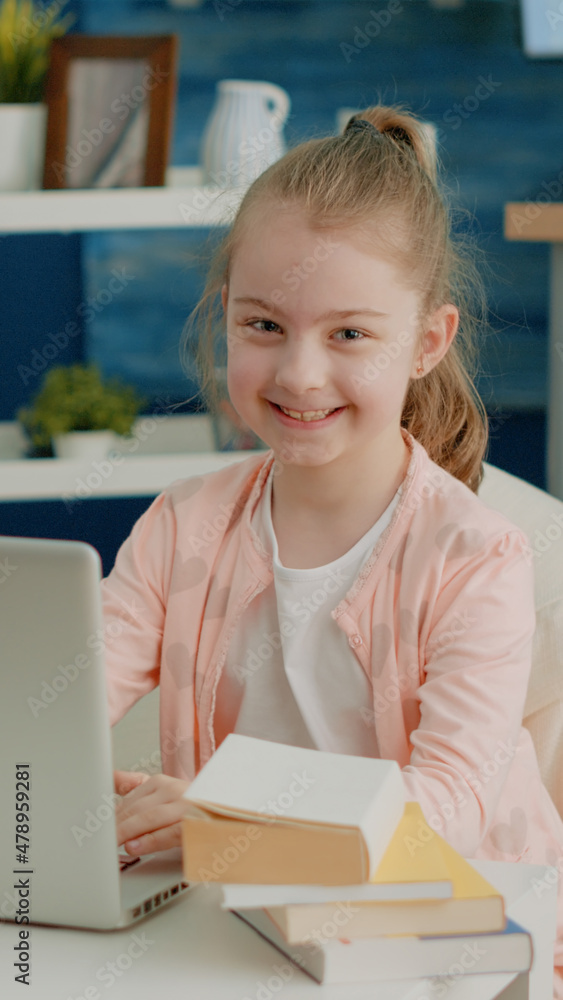 Poster portrait of schoolgirl using laptop for online school courses at home. little child smiling and look
