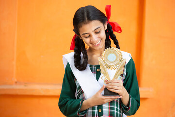 Young beautiful happy indian school girl celebrating victory with trophy,Cheerful braided female...