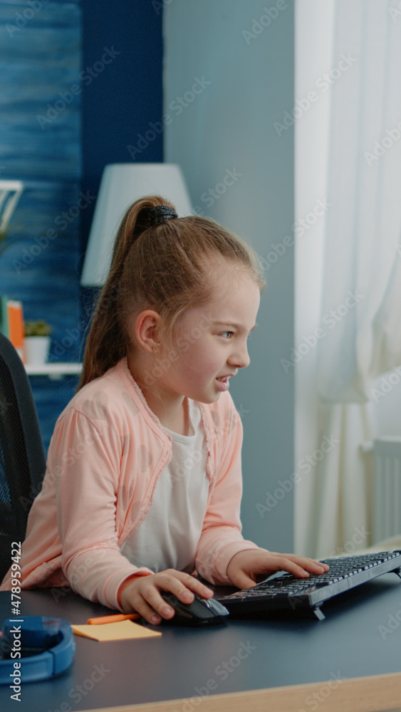Poster frustrated child using computer and keyboard for homework at home. little girl looking at monitor fo