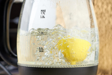 Half a yellow lemon is boiled in a glass electric kettle for descaling