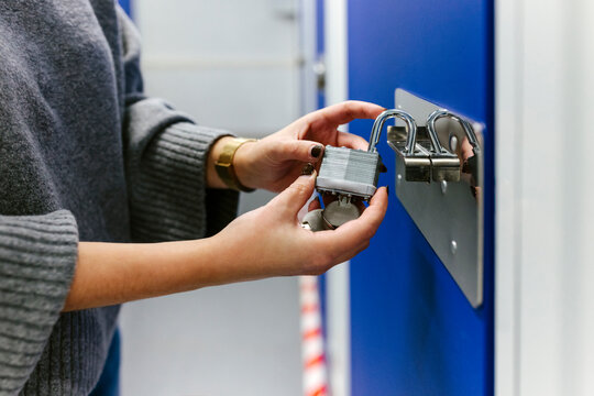 Anonymous woman opening padlocks on a blue door of a storage room