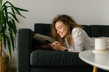 Woman laying on sofa and entertain with smartphone