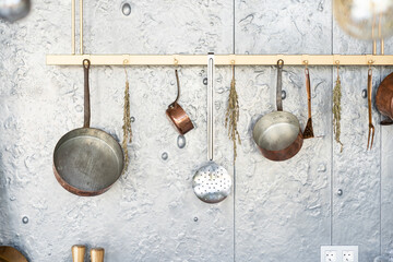 Set of saucepans hanging in kitchen. Hanging Copper kitchen utensil on the white wall. Different...