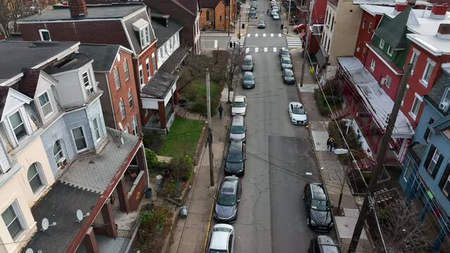 Rising aerial of homes in urban American town community neighborhood. Car drives on tight one-way street.