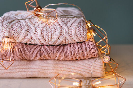 Stack of knitted sweaters with fairy lights garland.