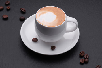 Coffee with milk, black background close. White cup of coffee with coffee beans on a black background.