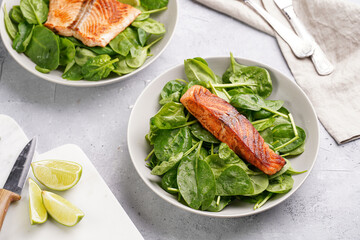 Grey bowl with fresh green raw spinach and fried red salmon, lime slices on grey concrete surface