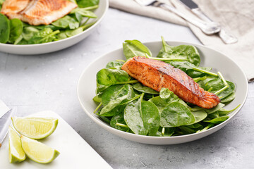 Grey bowl with fresh green raw spinach and fried red salmon, lime slices on grey concrete surface