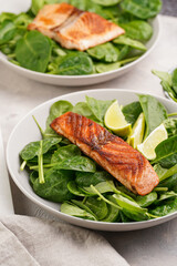 Grey bowl with fresh green raw spinach and fried red salmon, lime slices on grey concrete surface