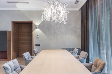 The interior of the dining room with a large table and chairs around the perimeter against a gray...
