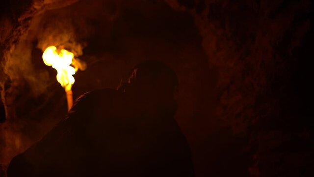 Young man exploring a dark cave with a burning torch