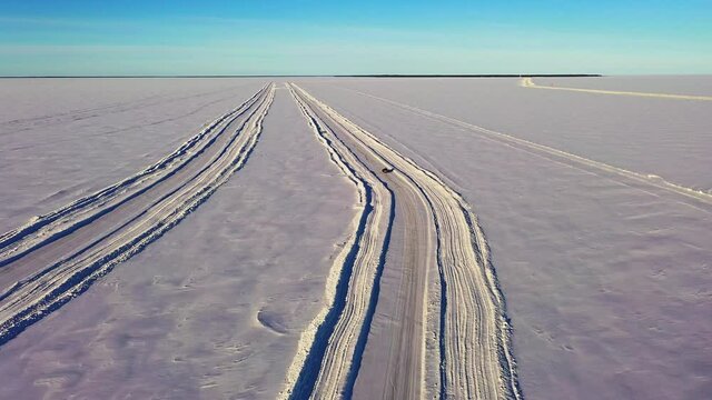 Aerial drone view following a car crossing arctic sea, through a ice bridge, during golden hour