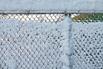 View of a frozen wire mesh fence covered with snow and ice on a bright sunny day. Background. Close-up. 