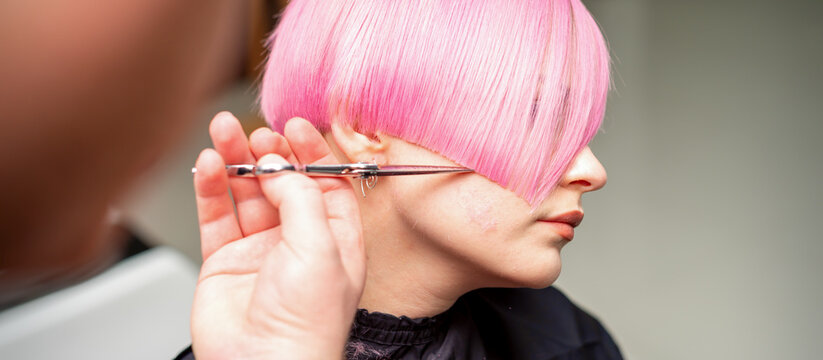 Hand of a hairdresser cutting short pink with scissor hair in a hairdressing salon, close up, side view