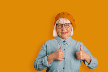 Portrait of caucasian 50s woman showing thumbs up good mood in studio isolated over bright orange color background