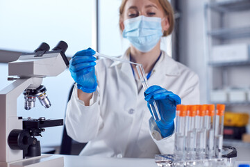 Female Lab Worker Wearing White Coat Using Pipette And Test Tube In Research