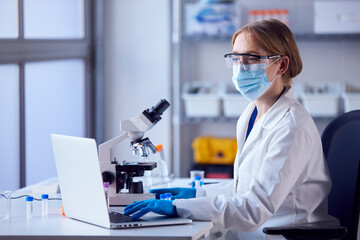 Female Lab Worker Wearing Lab Coat Analysing Samples In Laboratory With Laptop And Microscope