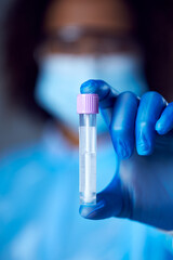 Female Lab Worker In PPE With Safety Glasses And Face Mask Holding Lateral Flow DNA PCR Test