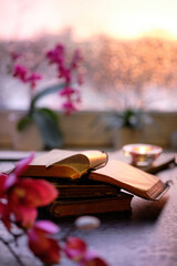 Wintertime with candle on stack of old books. Sunset window with orange glow, pink and fuchsia...