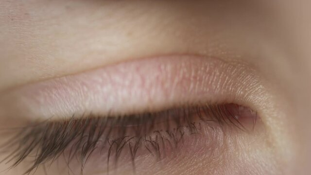 Extreme close-up of a beautiful girl's blue eye. Caucasian woman blinking an eye. Perfect clean young skin. Slow-motion.