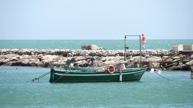Fishing boats near the pier, and man walking on the pier with strong wind in Minturno, Lazio, Italy.