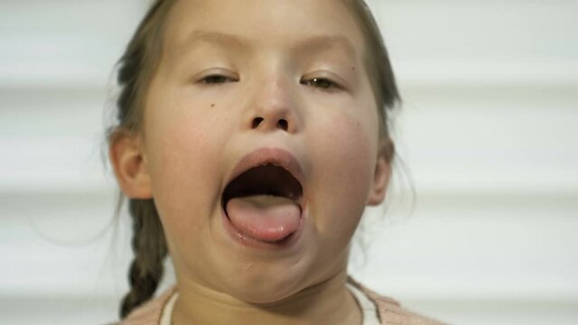 Girl of 7-8 years old diligently shows her tongue. Perhaps at a doctor's appointment.