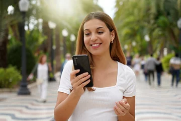 Poster Excited young woman watching her smartphone when walking in the street with blurred people on the background. Millennial girl using mobile app outdoors. Teenager lifestyle technology concept. © zigres