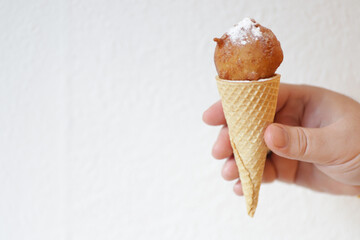 Hand holds horn with fried donut with sugar powder like ice-cream.