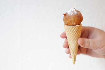 Hand holds horn with fried donut with sugar powder like ice-cream.