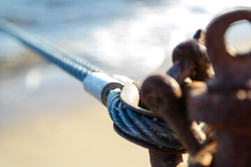 Close-up on the metal rope and rusty shackle. Sea in the background. 