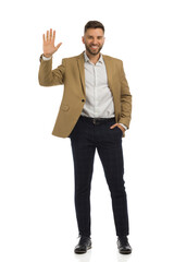 Elegant man in beige jacket is standing with hand raised. Front view. Full length isolated.
