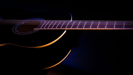 Fototapeta na wymiar black guitar on a dark background under beam of colored light with copy space. guitar music low-key concept