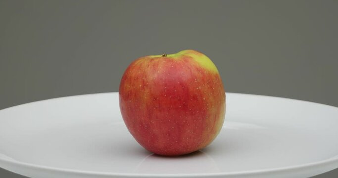 Fresh sweet red apple on a while plate spinning. Close up studio shot, isolated on gray background, real time, no people