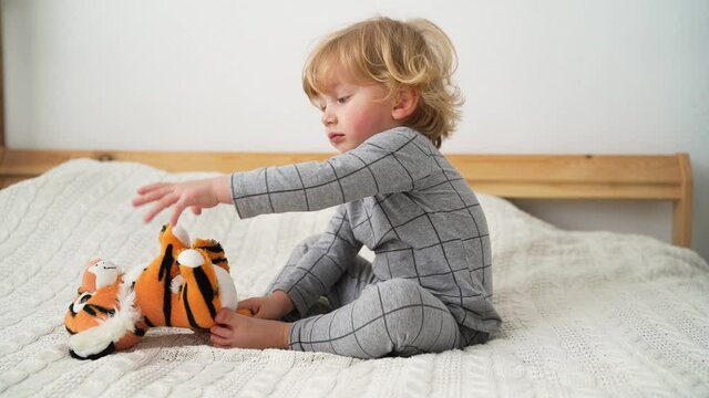 Portrait of little boy of two years old plays with toy tiger on the bed in cozy room Symbol of the year