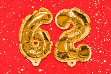 The number of the balloon made of golden foil, the number sixty-two on a red background with sequins. Birthday greeting card with inscription 62. Numerical digit, Celebration event, template.