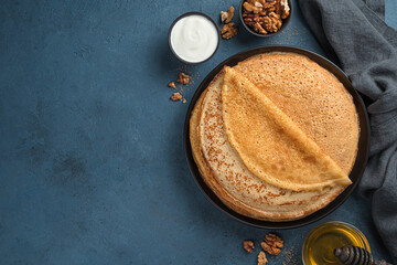 A stack of fried pancakes on a dark background with butter, honey and sour cream. Maslenitsa,...