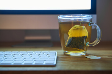 Work in the evening with a cup of tea with a visible tea bag. Keyboard and monitor out of focus....
