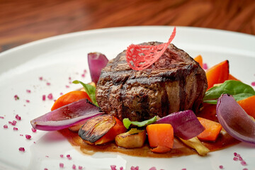 Beef fillet mignon with baked onions and vegetables in a white plate on a wooden background