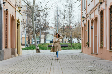Fototapeta na wymiar An adult woman in a beige coat and hat walking between buildings outdoors.
