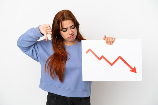 Young redhead woman isolated on white background holding a sign with a decreasing statistics arrow symbol and doing bad signal
