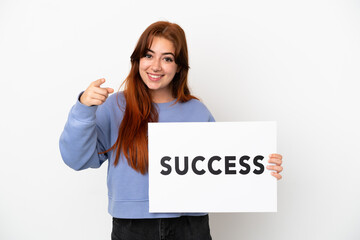 Young redhead woman isolated on white background holding a placard with text SUCCESS and pointing to the front