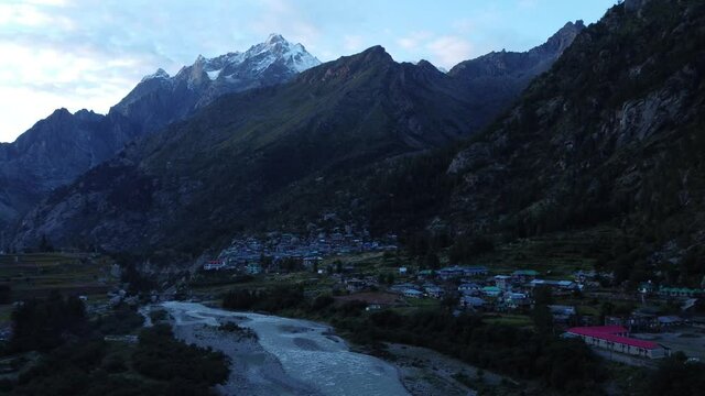 A drone shot of a  small scenic remote village on the banks of river Baspa with the snow peaks of Indian Himalayas in the background