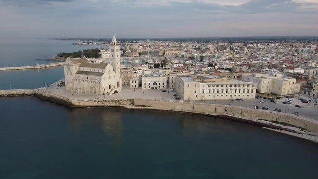 Zoom in aereo con drone su citt&agrave; Trani partendo dal mare adriatico mediterraneo della puglia verso la cattedrale e campanile, il porto sullo sfondo con le sue barche, yacht e il centro storico