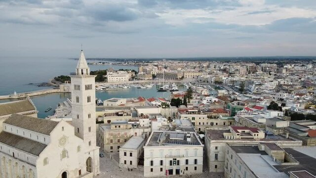 Panoramica aerea con drone su Trani, citt&agrave; della Puglia. Zoom out dal porto con barche, yacht, veliero, verso cattedrale e campanile con veduta della citt&agrave; dal mare adriatico in pomeriggio d'inverno