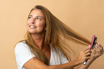 Middle age brazilian woman isolated on beige background with hair comb