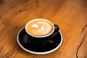 Latte arts coffe. Black cup of hot coffee on wooden table. Cafe with barista art concept.