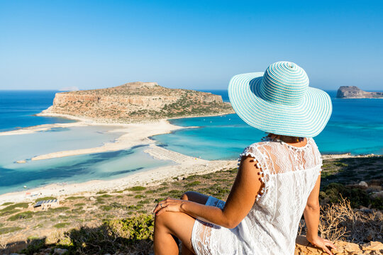 Portrait of woman with hat admiring the idyllic beach and lagoon sitting on top of hill, Balos, Crete, Greek Islands